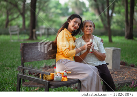 Young woman sitting beside an elderly woman with a jasmine garland after a Songkran blessing, portraying Thai family bonding, respect for elders, affection and authentic cultural tradition. Young woman sitting beside an elderly woman with a jasmine garland after a Songkran blessing, portraying Thai family bonding, respect for elders, affection and authentic cultural tradition. 138268072