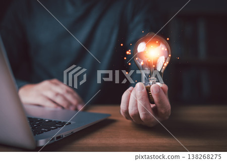A person hold a glow light bulb beside a laptop symbolizes creativity, innovation, and new ideas in technology and business development.Illustration of inspiration and digital transformation concept. A person hold a glow light bulb beside a laptop symbolizes creativity, innovation, and new ideas in technology and business development.Illustration of inspiration and digital transformation concept. 138268275