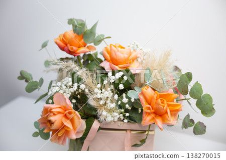 Macro view of orange rose petals surrounded by eucalyptus leaves and delicate white flowers in a floral arrangement. Natural beauty, botanical detail, floristry craft, romance, and celebration Macro view of orange rose petals surrounded by eucalyptus leaves and delicate white flowers in a floral arrangement. Natural beauty, botanical detail, floristry craft, romance, and celebration 138270015