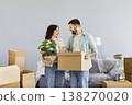 Happy family couple standing with moving box and houseplant in new apartment 138270020