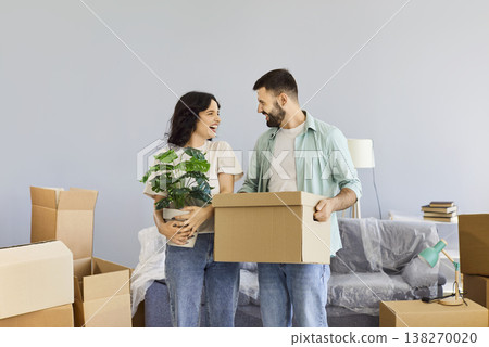 Happy family couple standing with moving box and houseplant in new apartment Happy family couple standing with moving box and houseplant in new apartment 138270020