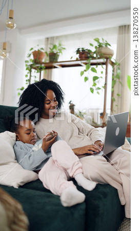 Mother and daughter multitasking in home living room 138270550
