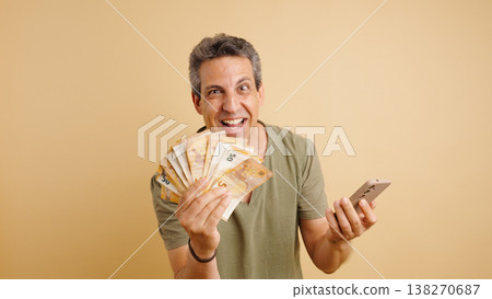 Excited man winning money holding Euros and smartphone Excited man winning money holding Euros and smartphone 138270687