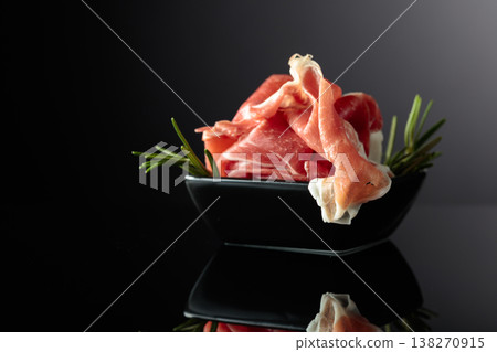 Prosciutto with rosemary on a black background. 138270915
