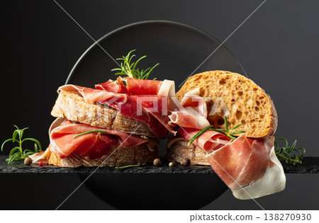 Ciabatta with prosciutto and rosemary on a black background. 138270930