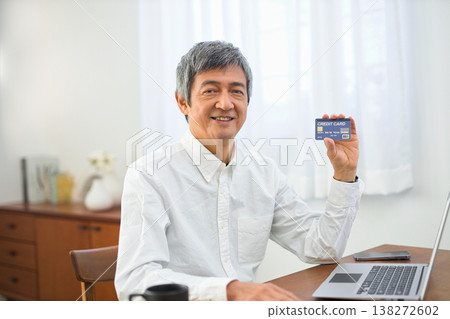 A man in his 60s looking at his computer and cards in the living room. 138272602