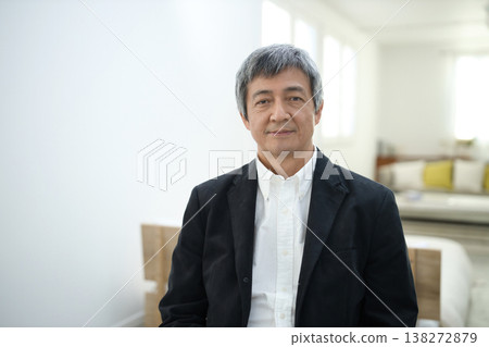 A man in his 60s wearing a jacket and with a serious expression in his room. 138272879
