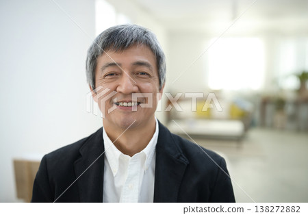 A man in his 60s wearing a jacket and smiling in his room. 138272882