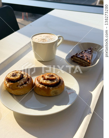 Coffee cup with foam and pastries with cake slice on tray in sunlight. Relaxation moment, cafe lifestyle, leisure break, enjoyment, calm atmosphere, everyday pleasure Coffee cup with foam and pastries with cake slice on tray in sunlight. Relaxation moment, cafe lifestyle, leisure break, enjoyment, calm atmosphere, everyday pleasure 138273280