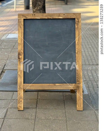 Blank black chalkboard sign standing on a city sidewalk near the street. Advertising space, urban commerce, pedestrian attention, and the clean potential of customizable storefront messaging. Blank black chalkboard sign standing on a city sidewalk near the street. Advertising space, urban commerce, pedestrian attention, and the clean potential of customizable storefront messaging. 138273289