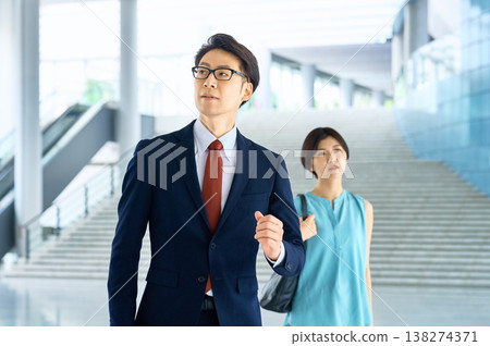 一位自信的日本商人與一位女士在辦公大樓裡徑直向前走去。 一位自信的日本商人與一位女士在辦公大樓裡徑直向前走去。 138274371