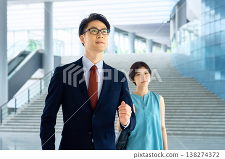 一位穿著西裝的商人與他的女同事快步走過一棟辦公大樓。 138274372