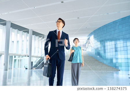 一位商人和一位女商人快步走過辦公大樓大廳。 一位商人和一位女商人快步走過辦公大樓大廳。 138274375