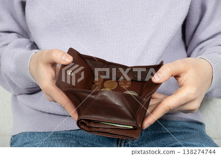 A woman holding an open leather wallet filled with various euro coins. A woman holding an open leather wallet filled with various euro coins. 138274744