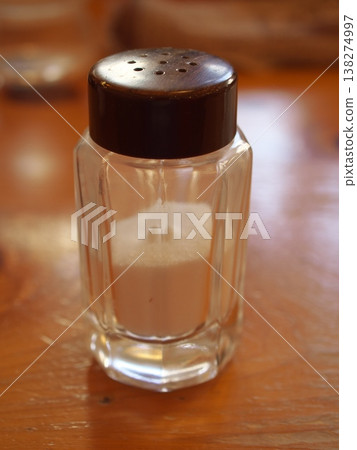 A glass salt shaker placed on a wooden table. A glass salt shaker placed on a wooden table. 138274997