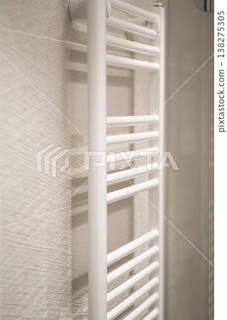 White modern heated towel rail hanging on a textured bathroom wall providing comfort and warmth in a contemporary and minimalist domestic interior White modern heated towel rail hanging on a textured bathroom wall providing comfort and warmth in a contemporary and minimalist domestic interior 138275305