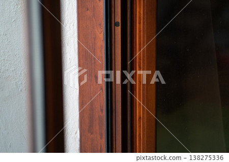 Wooden window frame with clear glass pane detailed against a white wall, showing interior architectural elements and a natural wood grain texture 138275336
