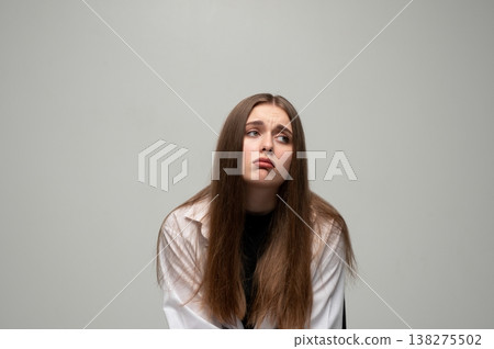 Young woman feeling upset and regretful, showing a disappointed and sad facial expression on a grey background 138275502