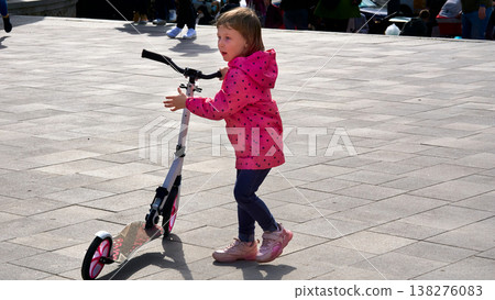 Cute active child rides a pink scooter in a city square Cute active child rides a pink scooter in a city square 138276083