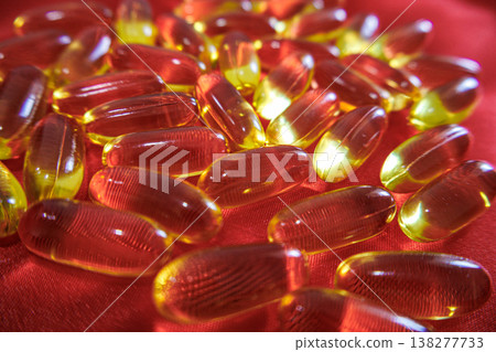 Soft focus fish oil capsules on red background. Omega 3 supplements and wellness concept with glowing translucent softgel pills. Soft focus fish oil capsules on red background. Omega 3 supplements and wellness concept with glowing translucent softgel pills. 138277733