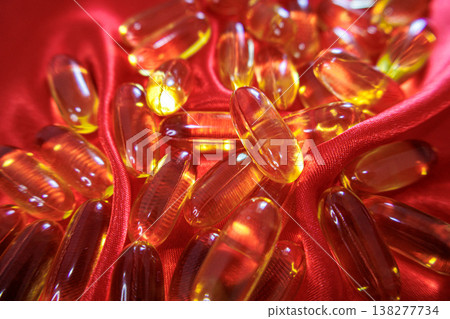 Golden fish oil capsules on red satin fabric with soft folds. Omega 3 supplements concept, health, wellness and nutrition background. Golden fish oil capsules on red satin fabric with soft folds. Omega 3 supplements concept, health, wellness and nutrition background. 138277734
