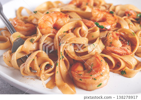 Fettuccine pasta with shrimp, spicy in soy sauce, on a grey plate with a fork, close-up, 138278917