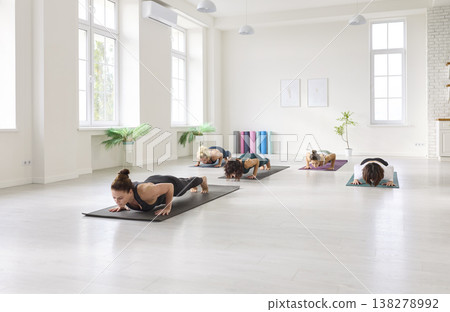Yoga class practicing chaturanga in minimalist studio, group women aligned on mats 138278992