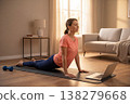 Woman performing cobra pose on yoga mat at home with laptop 138279668