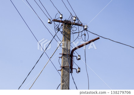 A strong electric pole stands against a blue sky, surrounded by tangled wires and vintage insulators, showcasing utility infrastructure A strong electric pole stands against a blue sky, surrounded by tangled wires and vintage insulators, showcasing utility infrastructure 138279706