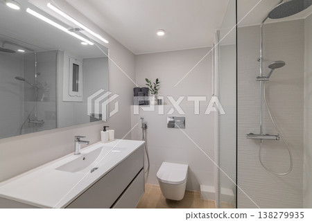 Modern bathroom with a sleek design. Features a white vanity, mirror, shower, and toilet. Bright lighting enhances the clean aesthetic. Modern bathroom with a sleek design. Features a white vanity, mirror, shower, and toilet. Bright lighting enhances the clean aesthetic. 138279935