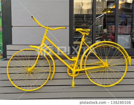Monochrome yellow bicycle mounted as storefront decoration against gray urban facade. Creative street display, city mobility symbol, recycled design object and eye catching exterior branding concept 138280108