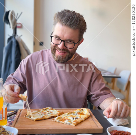 Smiling man lifting a slice of cheese turkish pide with melted topping in a bright cafe. Casual food enjoyment, authentic dining experience, weekend lunch mood and restaurant lifestyle scene 138280126