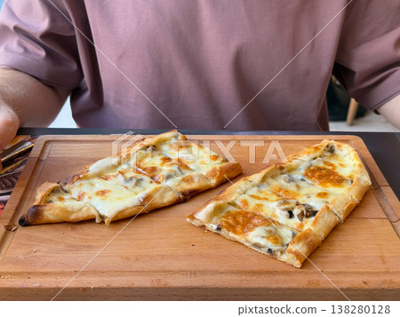 Cheese and mushroom pide portions served on a wooden board in a cafe setting. Baked flatbread menu item, casual restaurant dining and close food styling for hospitality promotion Cheese and mushroom pide portions served on a wooden board in a cafe setting. Baked flatbread menu item, casual restaurant dining and close food styling for hospitality promotion 138280128