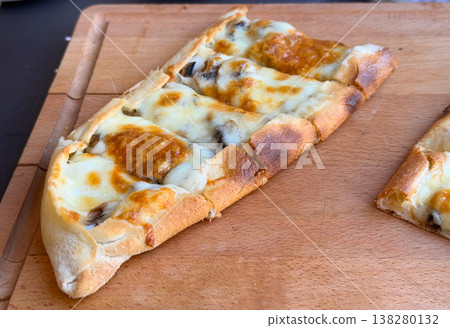 Closeup of a single cheese and mushroom pide slice with browned crust on a wooden board. Baked menu specialty, artisan flatbread detail and savory cafe food concept for restaurant promotion Closeup of a single cheese and mushroom pide slice with browned crust on a wooden board. Baked menu specialty, artisan flatbread detail and savory cafe food concept for restaurant promotion 138280132