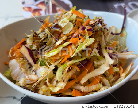 Mixed cabbage and carrot salad in a white bowl with glossy dressing and crisp texture. Fresh side dish, healthy restaurant serving and colorful vegetable accompaniment for everyday meals 138280141