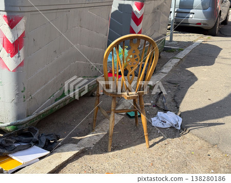 Abandoned wooden chair standing beside dumpsters and scattered litter in harsh sunlight. Urban neglect, illegal dumping, public sanitation issue and social documentary atmosphere in a backstreet Abandoned wooden chair standing beside dumpsters and scattered litter in harsh sunlight. Urban neglect, illegal dumping, public sanitation issue and social documentary atmosphere in a backstreet 138280186