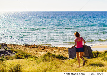 Woman on beach carrying deckchair Woman on beach carrying deckchair 138280595