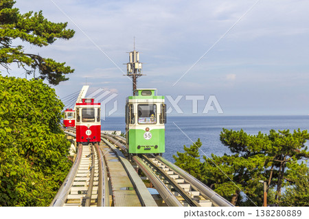 Colorful oceanfront capsule cars travel along an elevated coastal rail, offering scenic seaside views and a relaxed tourism experience over the water. High quality photo 138280889