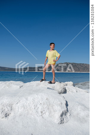 Young Boy Stands Confidently on a Rock Formation at a Sunny Beach With Clear Blue Waters in the Background 138281084