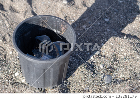 A Black Plastic Container Filled With Ice Cubes Sits on Sandy Ground Under Bright Sunlight During a Warm Outdoor Gathering A Black Plastic Container Filled With Ice Cubes Sits on Sandy Ground Under Bright Sunlight During a Warm Outdoor Gathering 138281179