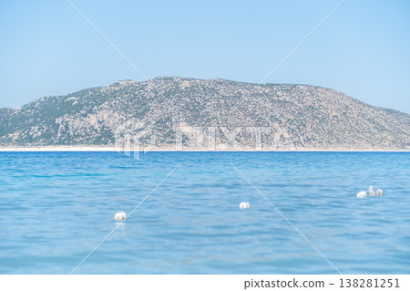 Clear Turquoise Water With Gentle Waves and Distant Rocky Hills Under a Bright Blue Sky at Midday 138281251