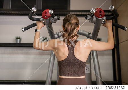 Strong Woman Performing Pull-Ups in Modern Gym During Afternoon Workout Session 138281282