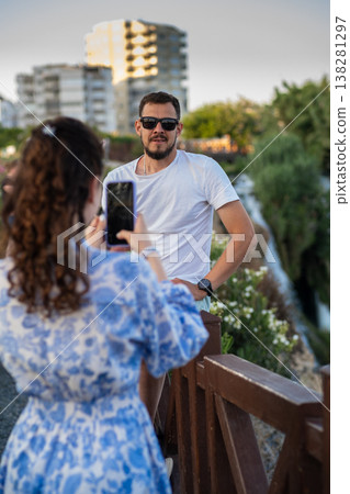 Couple Enjoying a Casual Moment Outdoors as One Takes a Phone Picture in a Relaxed Setting During Sunset 138281297