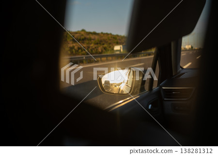 Reflections of a Road Trip Along the Highway at Sunset With Sunbeams Illuminating the Car Mirror 138281312