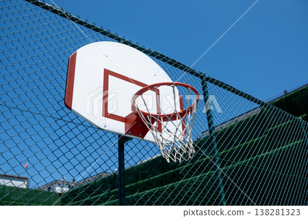 Basketball Hoop Attached to a Fence Under a Clear Blue Sky With a Few Clouds in the Background 138281323