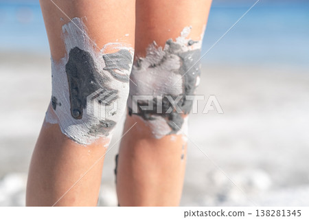 Woman Applying Clay Mask on Knees at the Beach During Sunny Day for Skin Care and Relaxation 138281345