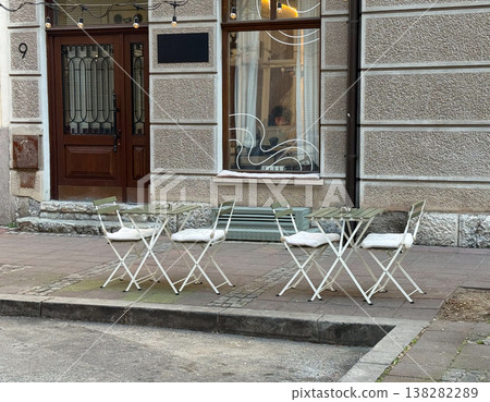 Outdoor seating stands beside a pastry and coffee shop facade. Urban pause, street hospitality, simplicity, neighborhood routine, and the inviting calm of everyday cafe culture. Outdoor seating stands beside a pastry and coffee shop facade. Urban pause, street hospitality, simplicity, neighborhood routine, and the inviting calm of everyday cafe culture. 138282289