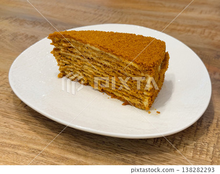 Honey cake slice on white plate with layered cream filling and crumb coating. traditional dessert, bakery product, pastry presentation, sweet indulgence, cafe serving, homemade recipe, comfort food 138282293