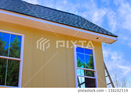 Worker installing yellow primed smooth siding house with tall windows, ladder in place Worker installing yellow primed smooth siding house with tall windows, ladder in place 138282519