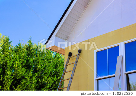 Contractor uses ladder to reach upper part of house under tasks installing premiered smooth fiber siding Contractor uses ladder to reach upper part of house under tasks installing premiered smooth fiber siding 138282520